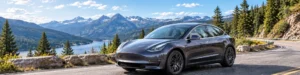 A dark electric vehicle driving along a scenic mountain road beside a lake.